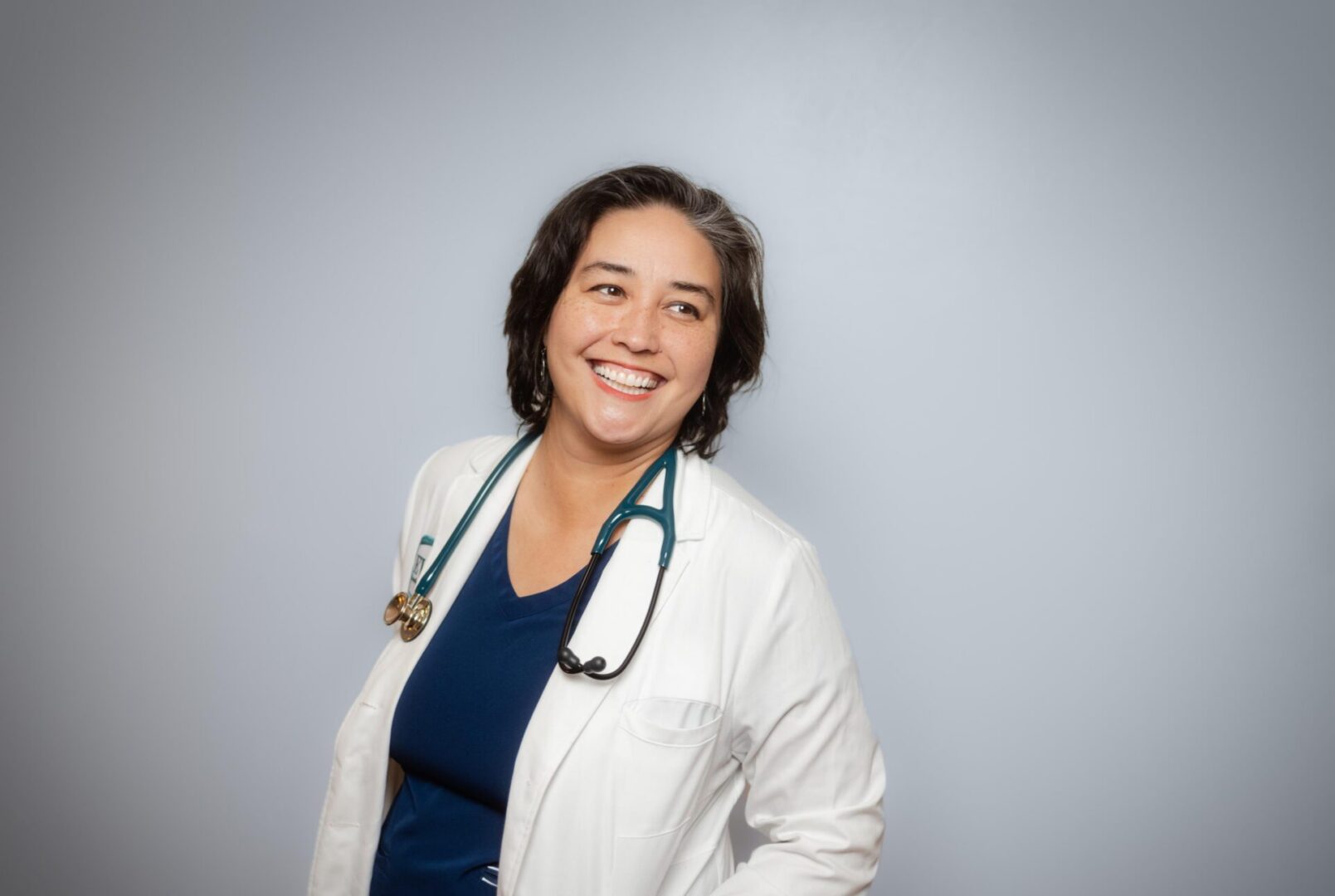 Smiling doctor with stethoscope against gray background.