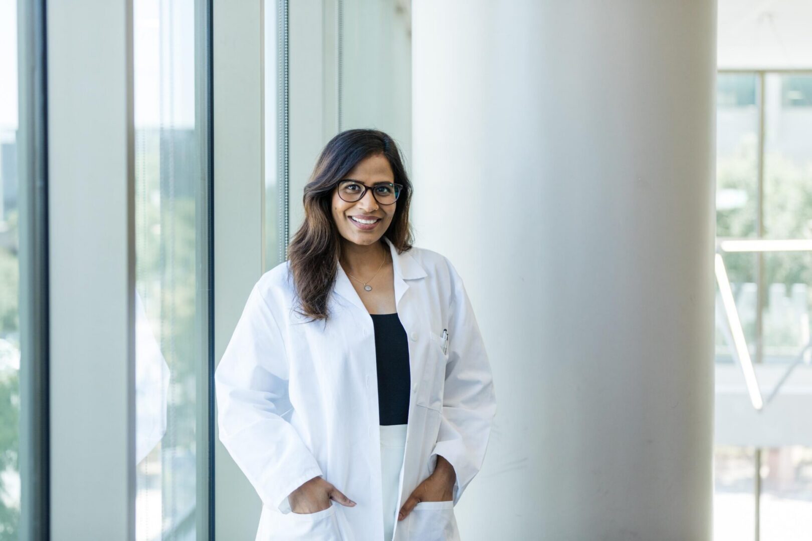 Person in lab coat near large windows.