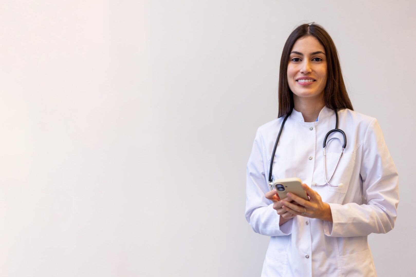 Smiling doctor with stethoscope holding phone.